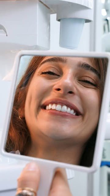 A patient seeing her new smile in a hand mirror